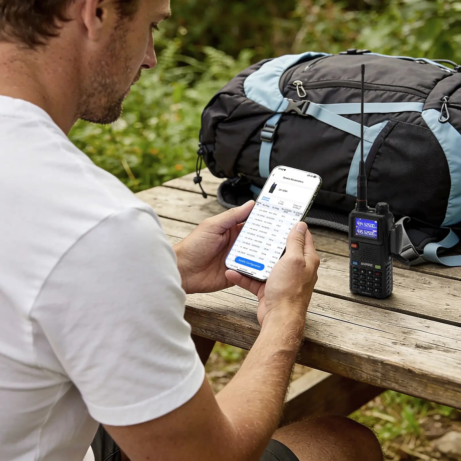 Man using a smartphone next to a walkie-talkie and backpack outdoors